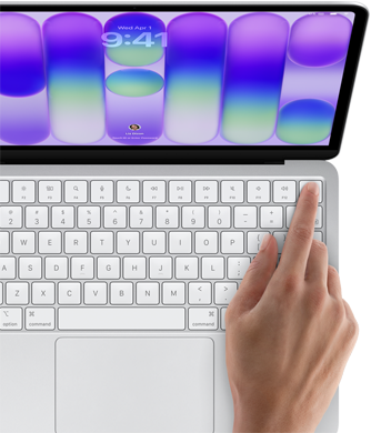 MacBook Neo, couleur argent, affichant l’écran de connexion, doigt d’une personne sur le capteur Touch ID situé dans le coin supérieur droit du clavier